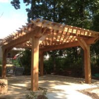 A custom pergola built from cedar stands strong, casting shadows from its lattice roof
