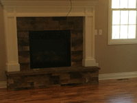 Stone fireplace with wooden mantle in room with medium stained wooden floors