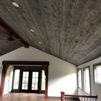 A vaulted ceiling is adorned with distressed, grey stained lumber, recessed lighting, and a central, dark cherry stained beam.